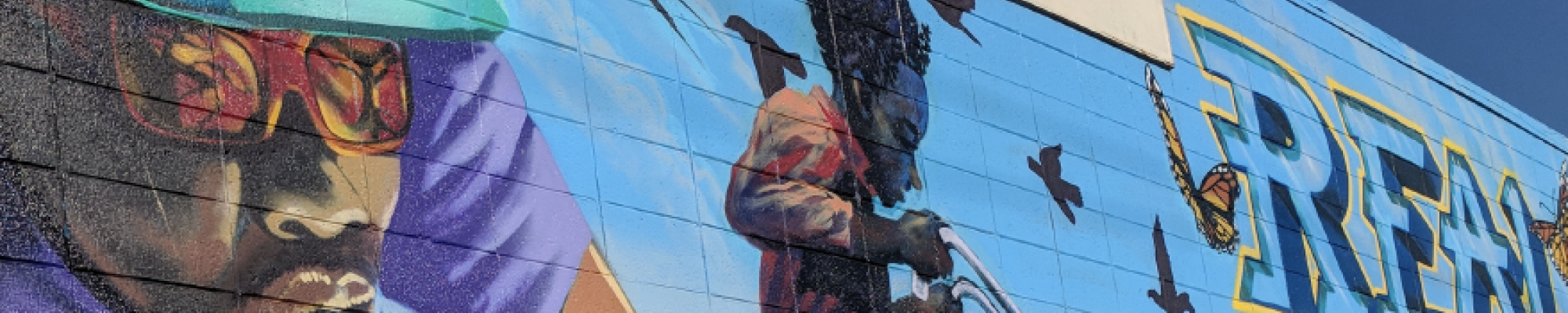 Street mural showing a Black man and young Black boy riding bikes; mural located on building of nonprofit Rich City Rides on MacDonald Avenue