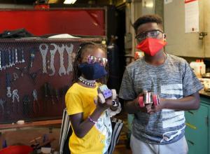 Two Black children standing in front of a wall of tools at The Crucible
