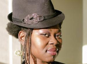 Headshot of The It Cast founder Nika Cherrelle. She is a Black woman, wearing a black fedora hat.