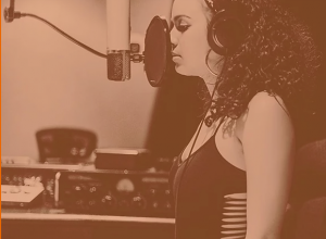 Photo of dark skinned teenage girl standing at a microphone.