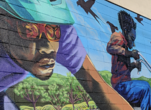 Street mural showing a Black man and young Black boy riding bikes; mural located on building of nonprofit Rich City Rides on MacDonald Avenue