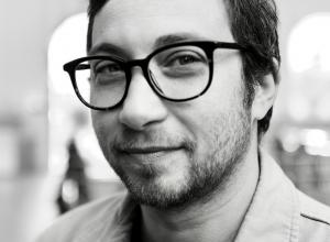 White male with dark rimmed glasses. He has short dark hair and a short beard.